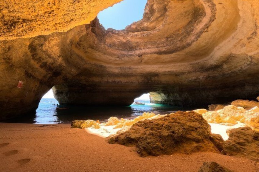 A large rock formation with a cave entrance and a sandy beach. 1