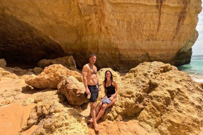 A man and a woman on a rocky beach with a large cliff in the background. 4