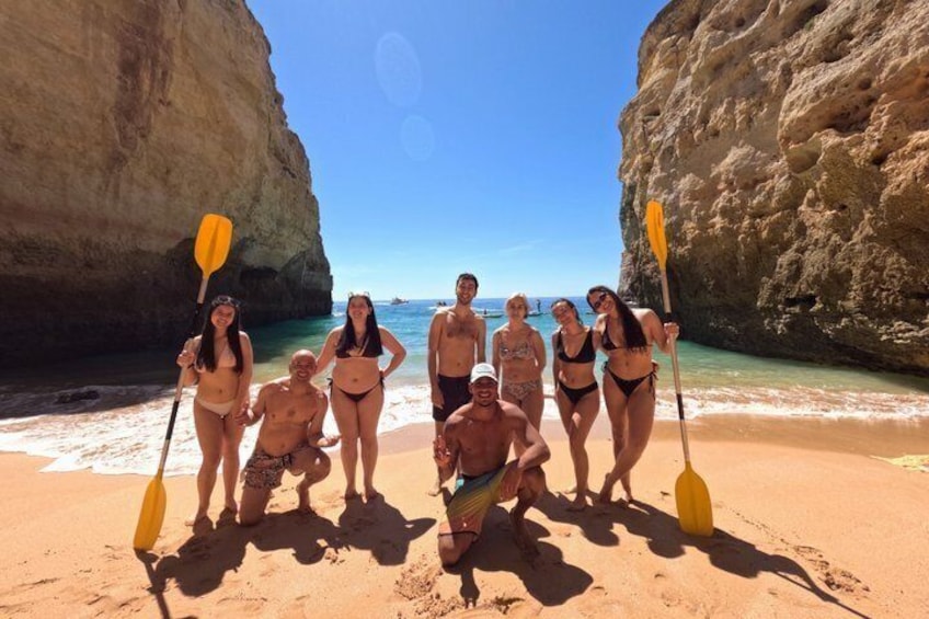 A group of people on a sandy beach with rocky cliffs and the ocean in the background. 2