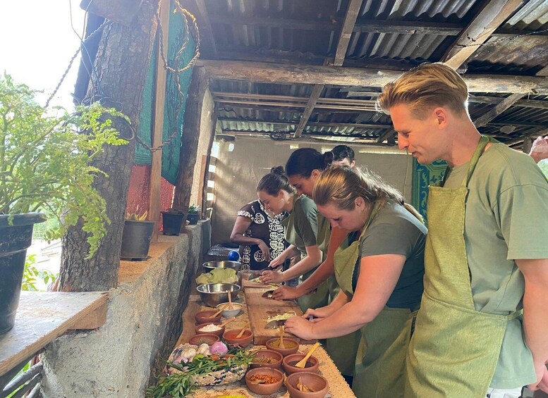 A group of people preparing food in a rustic kitchen with wooden beams and a corrugated metal roof. 5