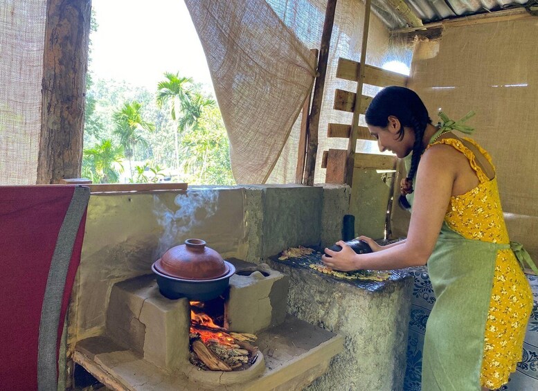 A person cooking outdoors using a traditional clay stove with a pot on top. 1