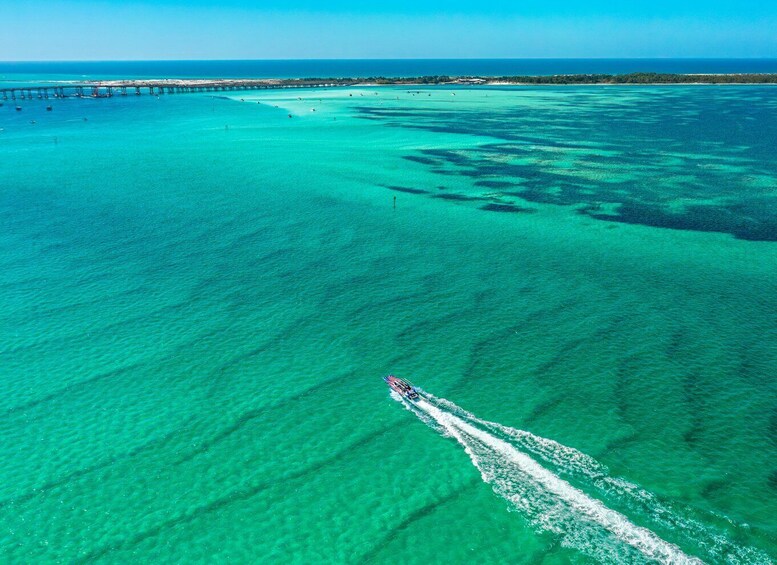A clear blue sea with a boat creating a wake, a pier extending into the water, and a distant shoreline. 5