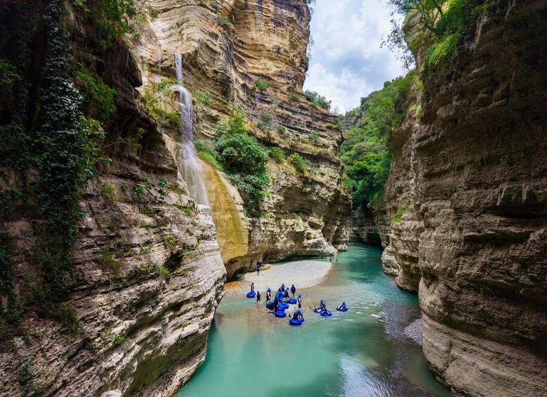 A canyon with a waterfall and people rafting in the river. 1