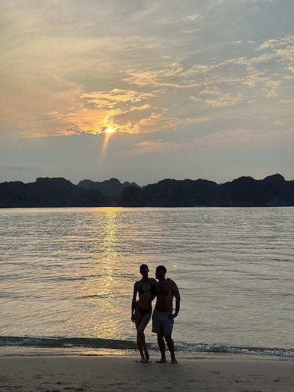 A couple standing on a beach with the sun setting in the background. 2