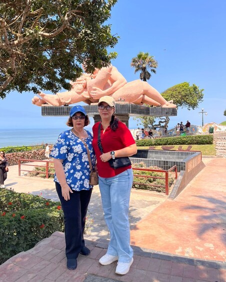 Two people standing in front of a large sculpture of a reclining figure. 2