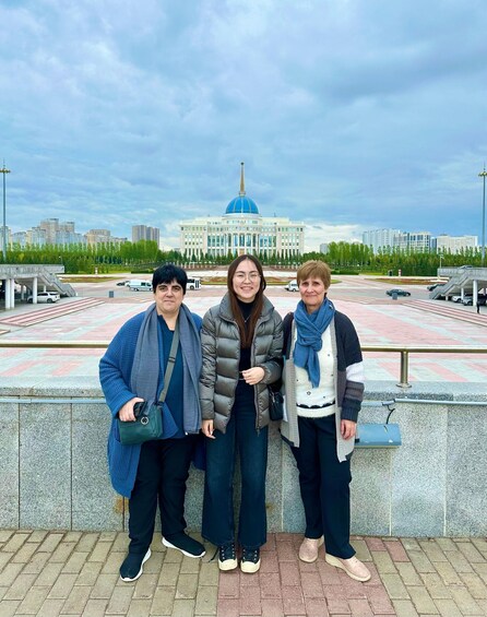 Three people standing in front of a building with a blue dome, surrounded by a paved area and trees. 3