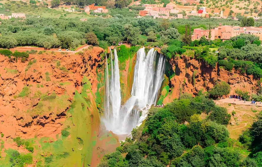 A large waterfall cascading down a steep cliff surrounded by greenery and buildings. 1