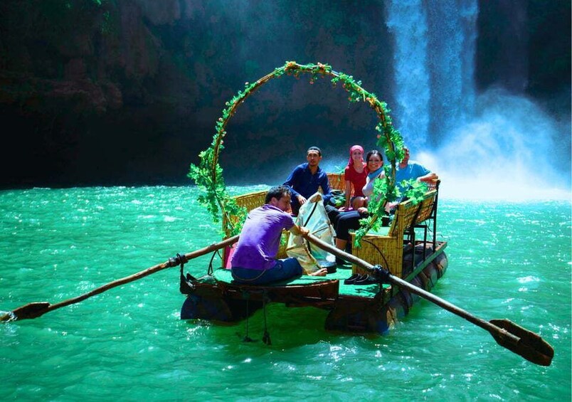 A boat with a decorative arch and passengers, surrounded by turquoise water and a waterfall. 3