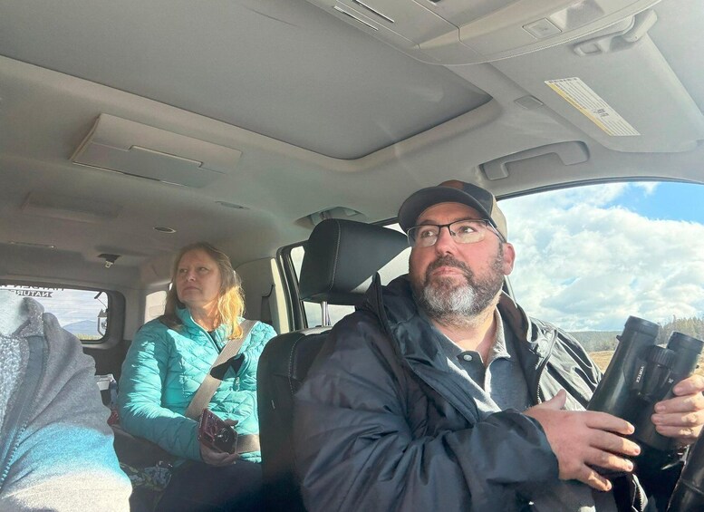 A vehicle interior with a person holding a camera and another person in a teal jacket. 3
