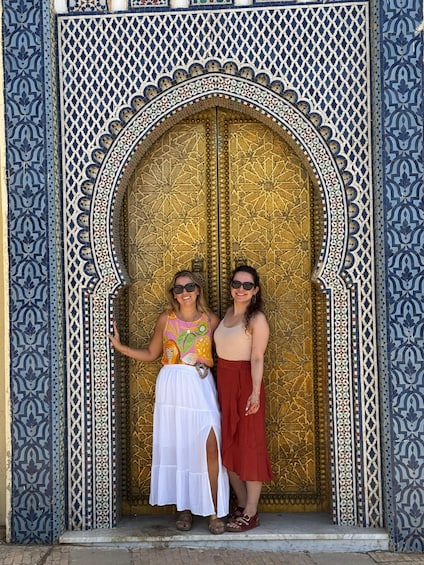 Two people standing in front of a large ornate door with intricate tile work. 1