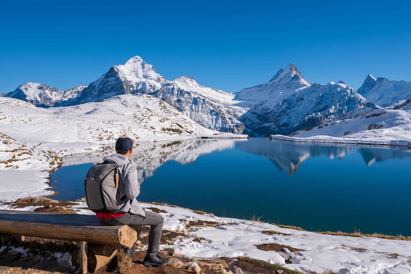A person sitting on a bench overlooking a calm lake with snow-covered mountains in the background. 3