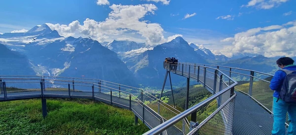 A metal walkway with a railing, overlooking a mountainous landscape with snow-capped peaks and a clear sky. 2
