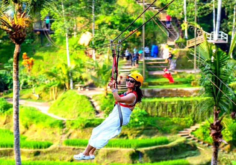 A person zip-lining through a lush, green landscape with terraced fields and a wooden bridge in the background. 4