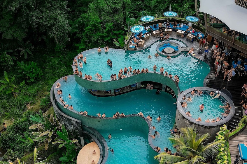 A large, winding pool surrounded by lush greenery and multiple seating areas. 1