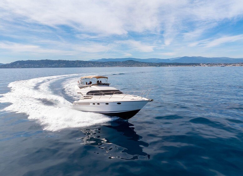 Un bateau à moteur blanc, doté d’un auvent, navigue sur des eaux bleues et calmes, avec une côte et des montagnes visibles au loin. 1