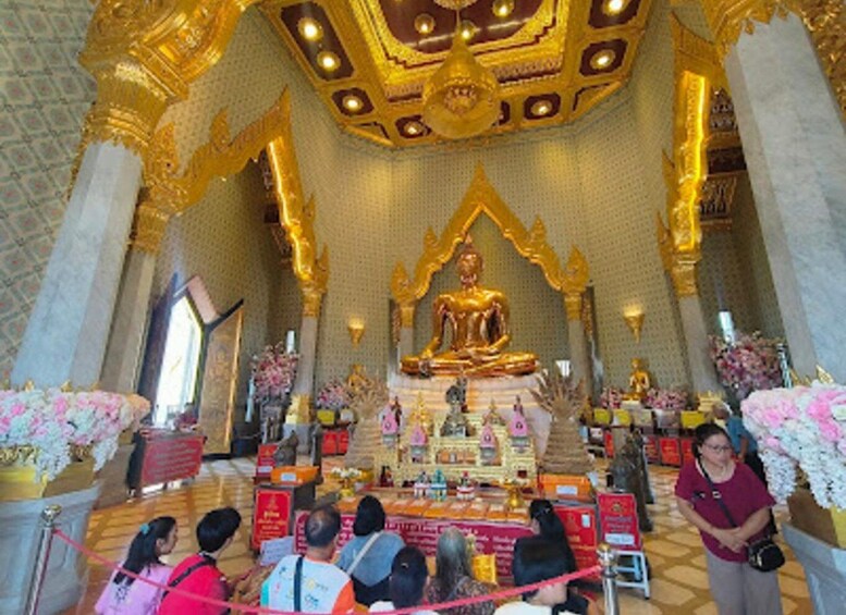 A golden Buddha statue in a temple with floral decorations and people around. 5