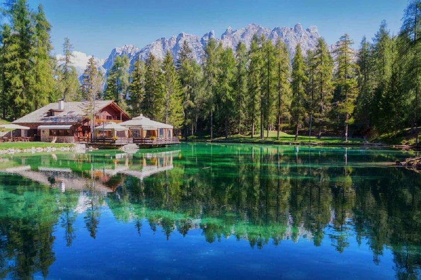 A lodge by a clear lake with reflections, surrounded by pine trees and mountains. 1