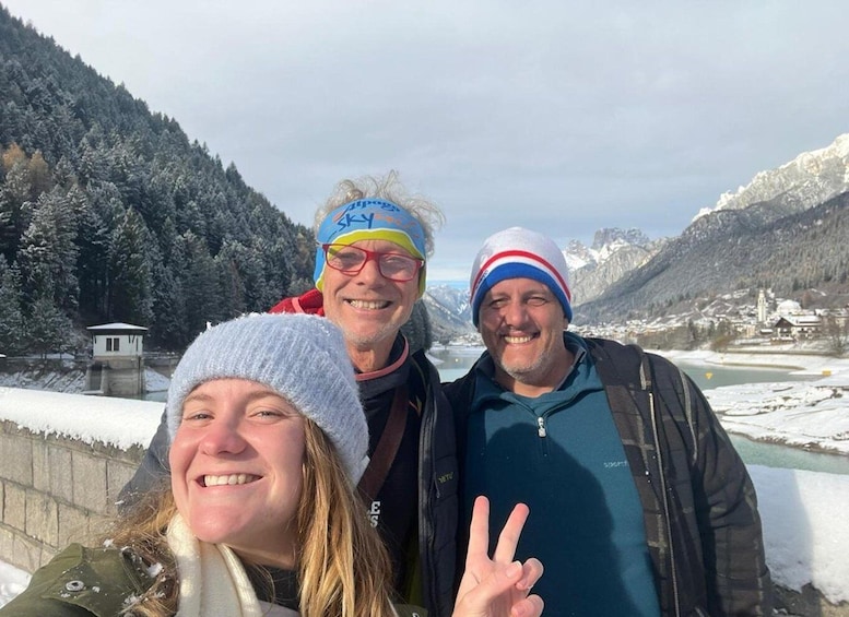Three people in winter clothing, a snowy landscape, a mountain, and a small building. 2
