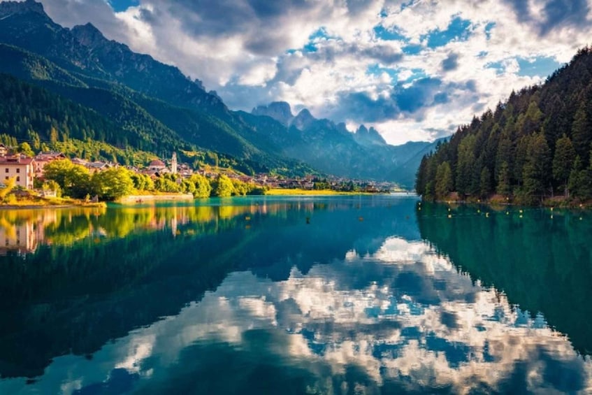 A calm lake reflecting mountains, a village with buildings, and dense forest. 3