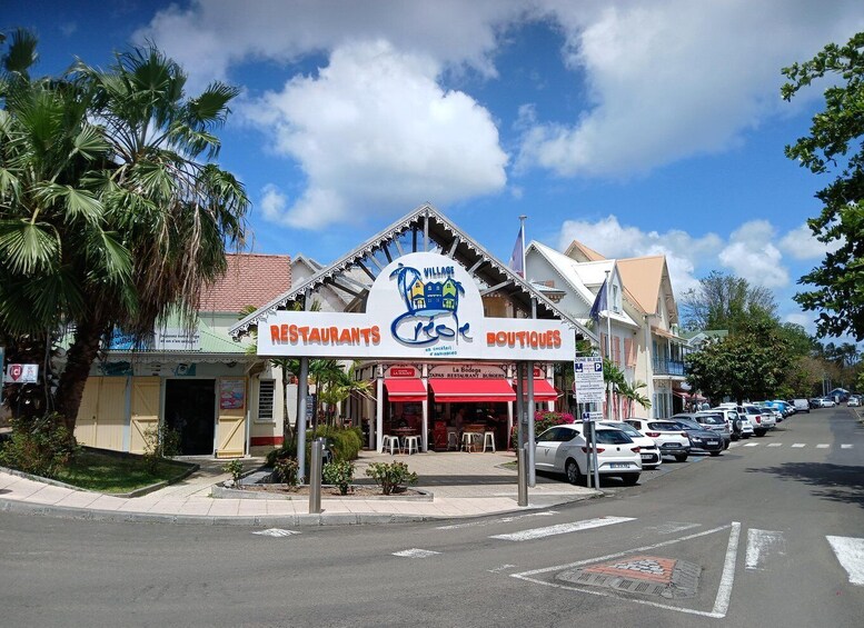 A street with a building labeled 'RESTAURANTS' and 'BOUTIQUES,' palm trees, parked cars, and a clear sky. 5