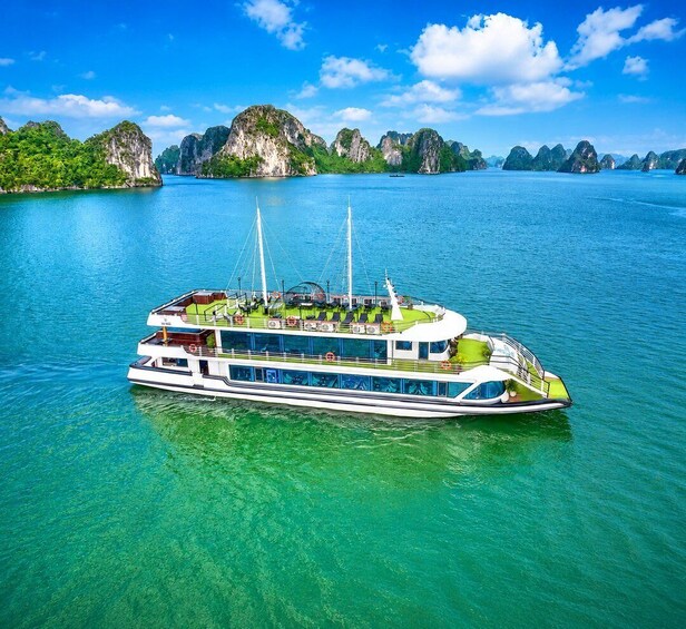 A large, multi-deck boat on clear turquoise water surrounded by lush green islands. 1