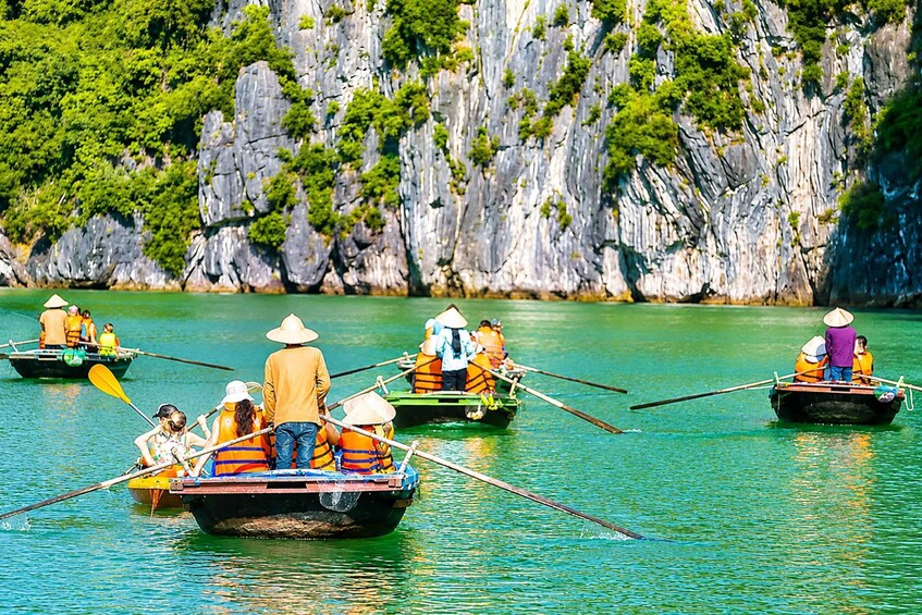 People paddling in traditional boats on a calm river, surrounded by rocky cliffs and lush greenery. 2
