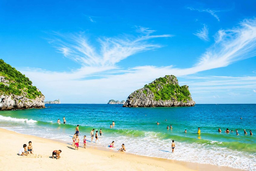 A beach with people swimming and walking along the shore, surrounded by clear blue water and green hills. 3