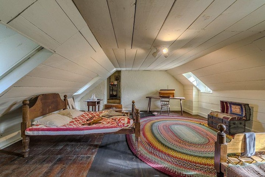 Une chambre à coucher aménagée dans un espace de type « loft », avec un plafond en bois, un lit, un tapis coloré et une petite table. 4