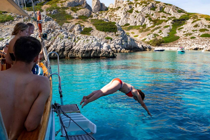 A person diving into clear blue water from a boat, rocky coastline, and a small boat in the distance. 3