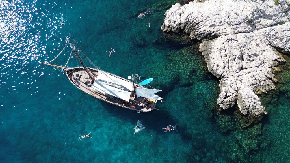 A sailboat anchored near rocky cliffs with clear turquoise water. 5