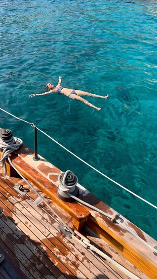 A person swimming in clear blue water, a rope, and a wooden deck with ropes and a life preserver. 3