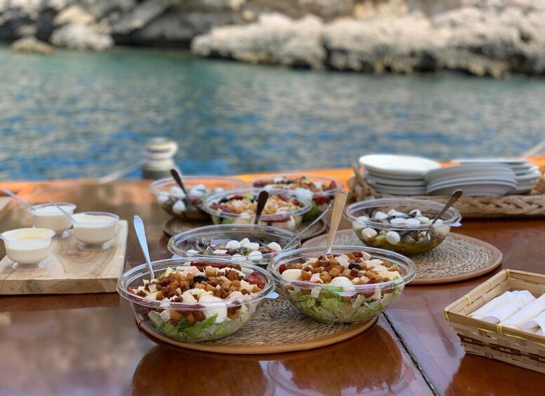 A table with various food items and bowls, set against a backdrop of a rocky shoreline and water. 2