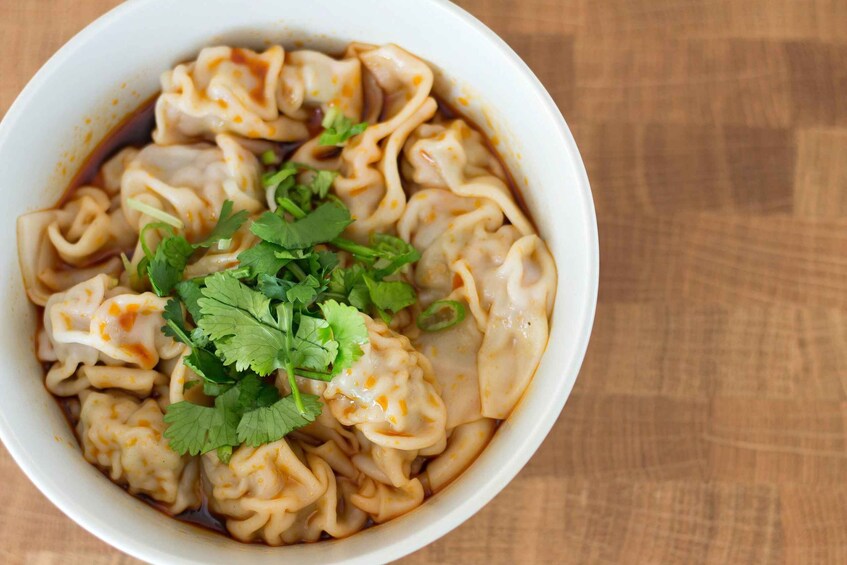 A bowl of dumplings in a broth, garnished with cilantro. 3