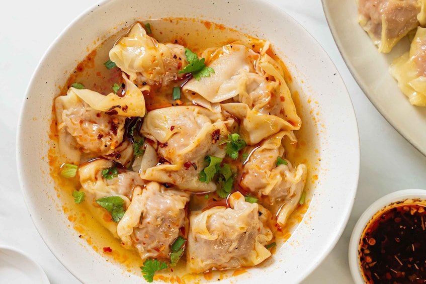 A bowl of dumplings in a spicy sauce with cilantro garnish. 1