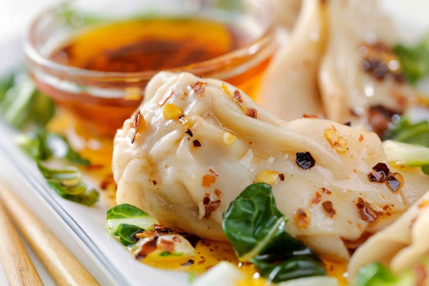 Dumplings garnished with chili flakes and greens, served with a dipping sauce. 4