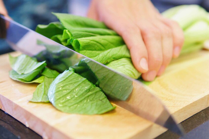 A person chopping green leafy vegetables on a wooden cutting board. 5