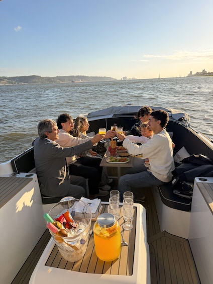 A group of people on a boat with a table set for a meal, a drink dispenser, and a view of the water and distant shoreline. 5