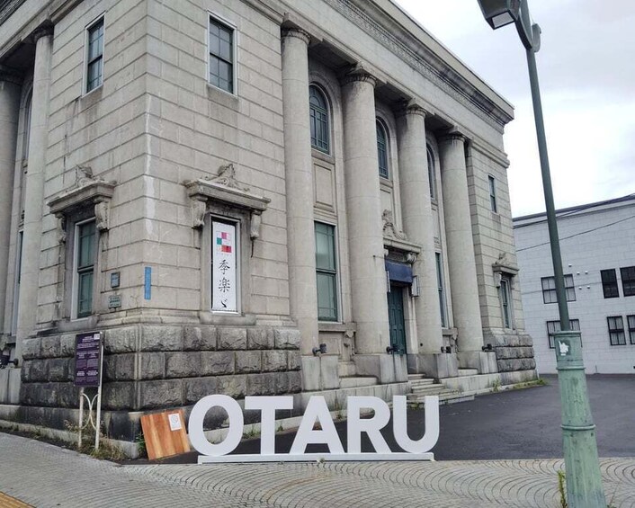 A large stone building with columns and a sign that reads 'OTARU.' 3