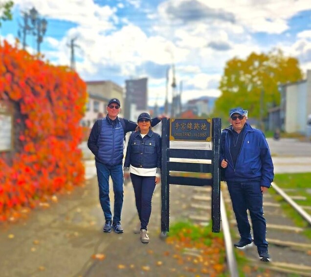 Three people standing in front of a sign with Japanese text. 1