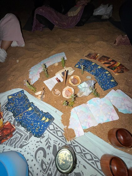 A tarot card spread on sand with a candle, shells, and a patterned cloth. 3