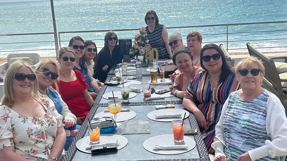 A group of people seated at a table on a boat with the ocean in the background. 1