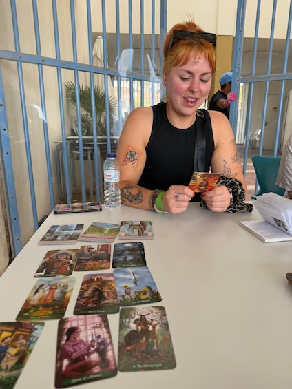 A person seated at a table with tarot cards, a smartphone, and a water bottle. 4