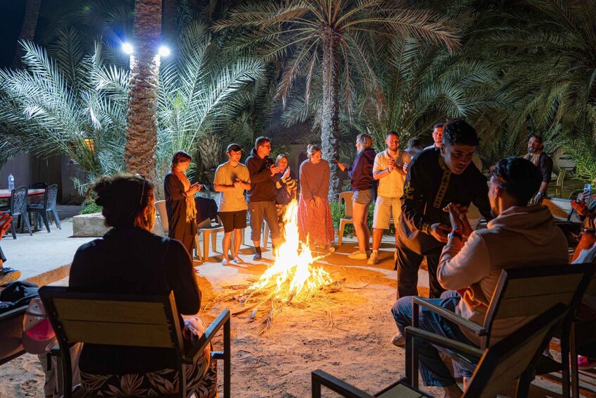 A group of people gathered around a campfire in an outdoor setting with palm trees. 3