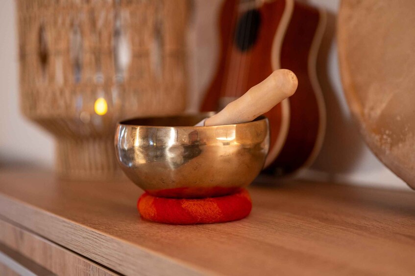 A brass bowl with a wooden mallet on a red base, a guitar, and a woven basket in the background. 5