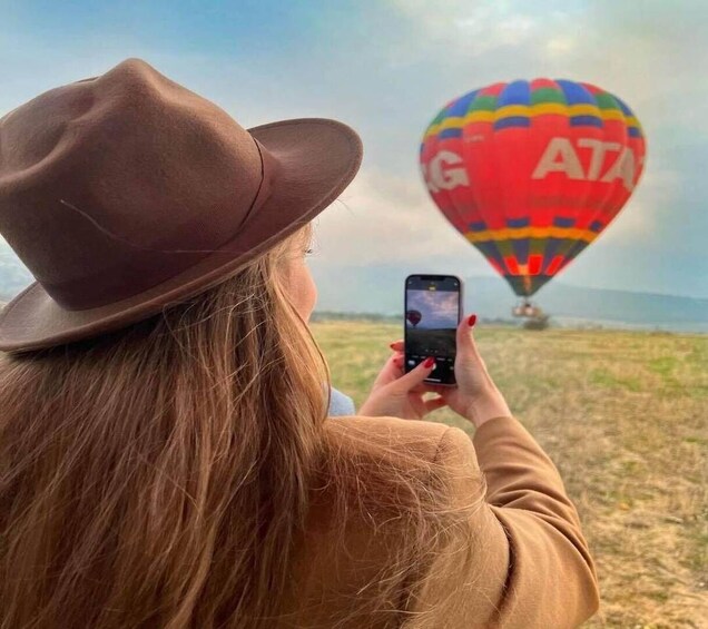 A person taking a photo of a colorful hot air balloon with 'ATA' written on it. 3