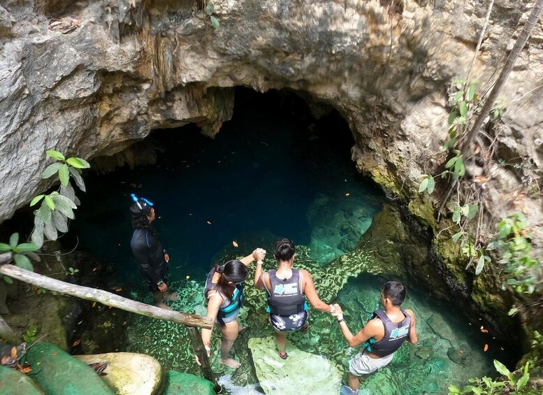A group of people in a cave with clear water, surrounded by rocky walls and greenery. 2