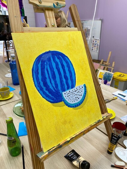 An easel with a painting of a blue watermelon on a yellow background. 5