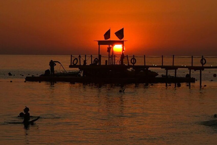 A sunset over a pier with boats and a person in the water. 2