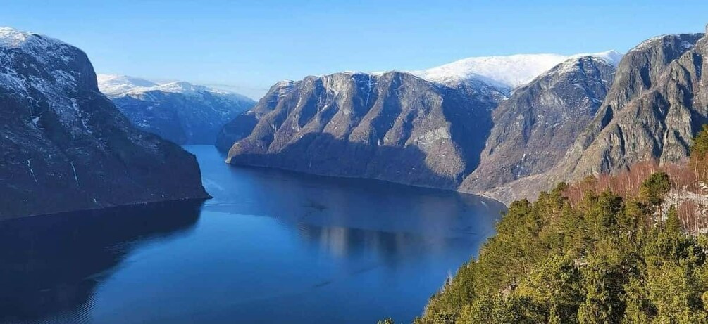 A fjord surrounded by mountains with snow-capped peaks and dense forest. 2