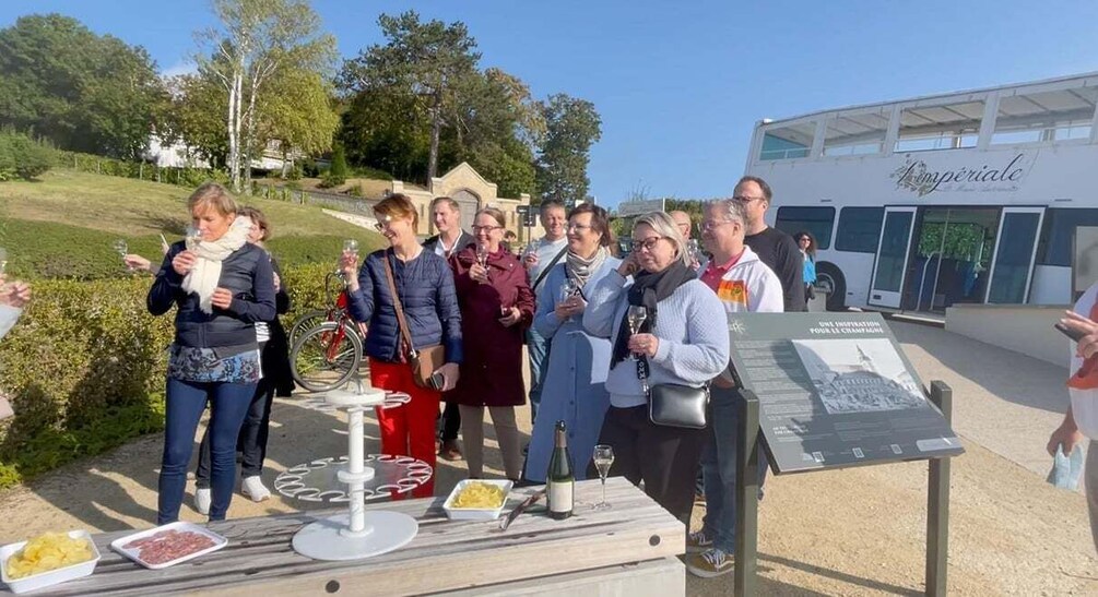 A group of people at an outdoor event with a table displaying food and wine. 4